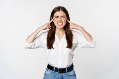 Annoyed girl shut ears from loud sound, discomfort of hearing smth noisy, standing bothered against white background