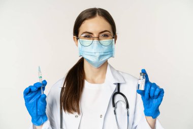 Covid-19 aşı ve sağlık hizmeti konsepti. Tıbbi maskeli genç doktor beyaz arka planda duran Coronavirus omicron varyasyonundan şırınga ve aşı gösteriyor.