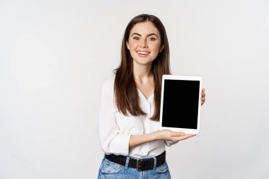 Portrait of corporate woman showing tablet screen, demonstrating company website, standing over white background