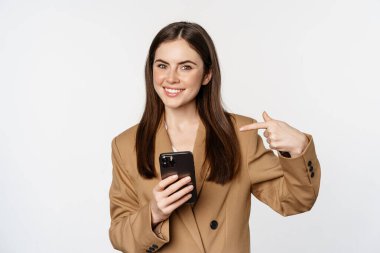 Hevesli satıcı, iş kadını cep telefonunu işaret eden ve gülümseyen, cep telefonuyla konuşan, beyaz arka planda duran.
