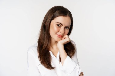 Close up of beautiful, coquettish brunette woman, blushing and smiling flirty, posing against white background