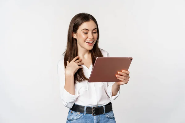 Porträt eines schönen Mädchens, das lächelt, glücklich aussieht, auf einem digitalen Tablet zusieht, vor weißem Hintergrund steht — Stockfoto