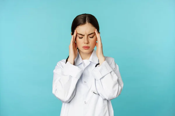 Изображение женщины-врача, медицинский персонаж, корчащийся от дискомфорта, страдающий головной болью, мигренью, чувствующий себя изможденным, стоящий на торкизном фоне — стоковое фото