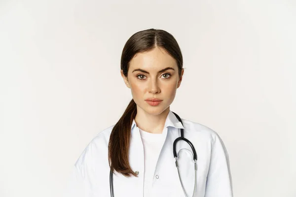 Zbliżenie portret, twarz młodej kobiety lekarz ze stetoskopem, wygląda poważnie, profesjonalny pracownik służby zdrowia w klinice, stoi na białym tle — Zdjęcie stockowe