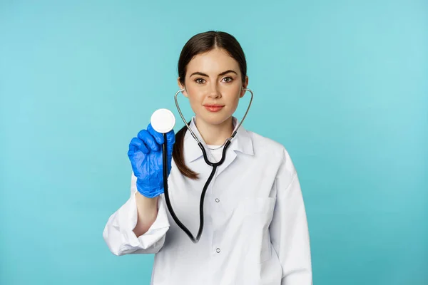 Image of woman doctor, listening patient lungs with stethoscope, doing medical checkup in clinic, standing over blue background — ストック写真