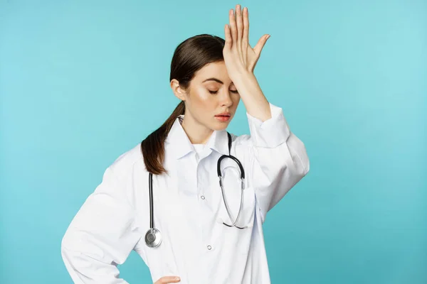 Retrato de médico mujer molesto, cansado, facepalm, rollo de ojos frustrados, molestado por smth estúpido, de pie en capa blanca sobre fondo de color turquesa — Foto de Stock