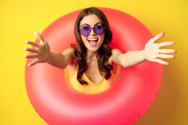 Close up portrait of beautiful happy woman inside pink swimming ring, luring, inviting people on summer vacation, beach party, standing over yellow background
