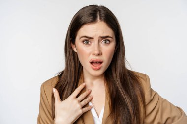 Shocked, offended businesswoman pointing at herself, looking insulted and hurt, arguing, standing against white background