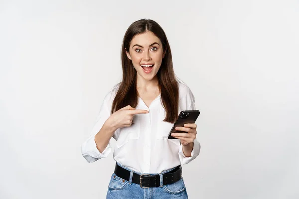 Nadšená dívka ukazuje prstem na smartphone a usmívá se, ukazuje velký prodej on-line, pomocí aplikace na mobilním telefonu, bílé pozadí — Stock fotografie