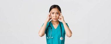 Sağlık çalışanları, virüsü önleme, karantina kampanyası konsepti. Yorgun Asyalı kadın doktor, başı dönüyor, dokunuyor, baş ağrısı çekiyor, beyaz arka planda duruyor.