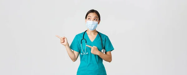 Covid-19, coronavirus disease, healthcare workers concept.兴奋而惊奇的亚洲女医生，戴着医疗面罩和手套的医生，手指指向左上角，白色背景 — 图库照片