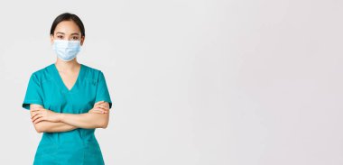 Covid-19, koronavirüs hastalığı, sağlık çalışanları konsepti. Gülümseyen, kendine güvenen Asyalı kadın doktor, check-up yapan doktor, önlük ve tıbbi maske takan, kararlı görünen, beyaz arka plan