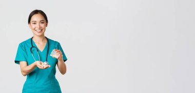 Sağlık çalışanları, virüsü önleme, karantina kampanyası konsepti. Gülümseyen Asyalı doktor, önlüklü doktor, hastaya konteynırdan beyaz arka plan ilacı veriyor.