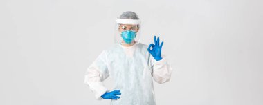 Covid-19, koronavirüs hastalığı, sağlık çalışanları konsepti. Kişisel koruma ekipmanları içinde ciddi görünümlü Asyalı kadın doktor, iyi bir jest gösteriyor, hastanın güvenliğini sağlıyor.
