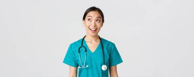 Sağlık çalışanları, virüsü önleme, karantina kampanyası konsepti. Hevesli gülümseyen Asyalı doktor önlüklü, hemşire sol üst köşeye bakıyor, yüzü gülmüş, beyaz arka planda duruyor.