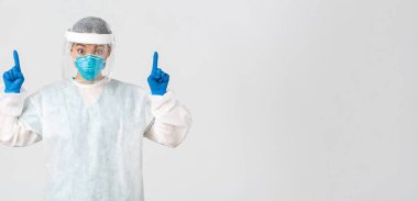 Covid-19, koronavirüs hastalığı, sağlık çalışanları konsepti. Şaşırmış ve şaşırmış Asyalı kadın doktor, solunum cihazları ve kişisel koruma ekipmanları ile reklamları işaret ediyor.