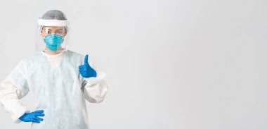 Covid-19, koronavirüs hastalığı, sağlık çalışanları konsepti. Kişisel koruma ekipmanları içinde ciddi görünümlü Asyalı kadın doktor, baş parmağını kaldırıyor, hastanın güvenliğini sağlıyor.
