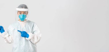 Covid-19, koronavirüs hastalığı, sağlık çalışanları konsepti. Şaşırmış kadın Asyalı doktor, tıbbi solunum cihazı hekimi ve sol üst köşeyi gösteren kişisel koruyucu ekipman.