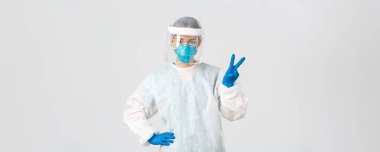 Covid-19, koronavirüs hastalığı, sağlık çalışanları konsepti. Küstah Asyalı kadın doktor, doktor ya da teknoloji laboratuarı kişisel koruma ekipmanları barış işareti gösteriyor, beyaz arka plan