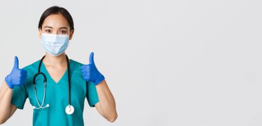 Covid-19, koronavirüs hastalığı, sağlık çalışanları konsepti. Kendinden emin gülümseyen Asyalı doktor, tıbbi maske takan hemşire ve lastik eldiven, onaylama için onay ver, hizmet et, bilgi topla.