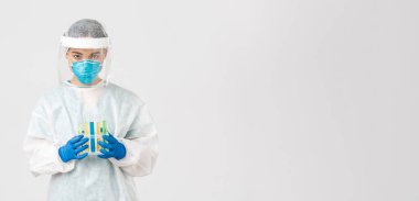Covid-19, koronavirüs hastalığı, sağlık çalışanları konsepti. Ciddi görünümlü Asyalı kadın laboratuvar çalışanı, kişisel koruma ekipmanları araştırmacısı, aşı ile test tüpleri tutuyor.