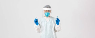 Covid-19, koronavirüs hastalığı, sağlık çalışanları konsepti. Şaşırmış ve heyecanlı Asyalı doktor, kişisel koruyucu ekipman enfeksiyonisti, elinde şırınga ve aşı ampulü var.