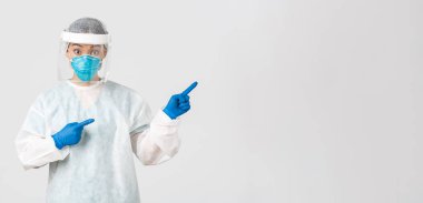 Covid-19, koronavirüs hastalığı, sağlık çalışanları konsepti. Şaşırmış ve şaşırmış Asyalı kadın doktor, kişisel koruma ekipmanları içinde teknoloji laboratuarı çalışanı şaşırmış ve parmağıyla işaret ediyor.