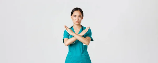 Covid-19, sjukvårdspersonal, pandemikoncept. Missnöjd allvarlig oro asiatisk kvinnlig läkare visa kors gest, vill att du sluta, förbjuda eller förbjuda farliga åtgärder, vit bakgrund — Stockfoto