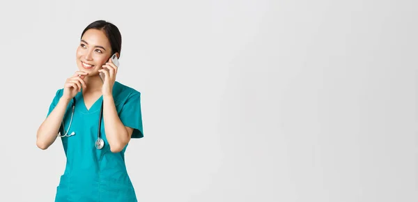 Covid-19, sağlık çalışanları ve virüs konseptini önlemek. Gülümseyen Asyalı kadın doktor portresi, önlüklü stajyer telefonla konuşuyor ve düşünceli görünüyor, düşünüyor ya da seçim yapıyor. — Stok fotoğraf
