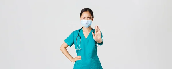 Covid-19, choroba koronawirusowa, koncepcja pracowników służby zdrowia. Poważny wygląd niezadowolony azjatycki lekarz, pielęgniarka w fartuchu zatrzymuje cię, pokazać zakazać, gest ostrzegawczy, zabronić pacjenta — Zdjęcie stockowe