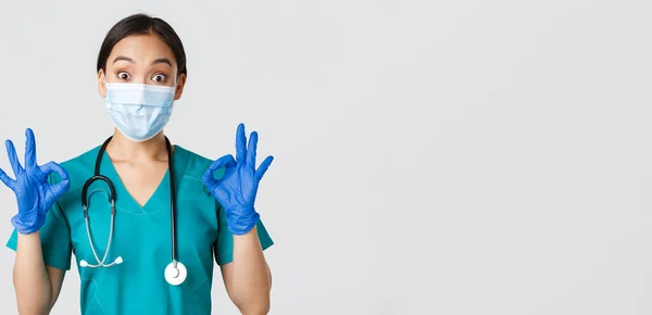 Covid-19, onemocnění koronavirem, koncept zdravotnických pracovníků. vzrušený a ohromen asijský lékař, zdravotní sestra v lékařské masce a gumové rukavice ukazující v pořádku gesto, schvalovat nebo chválit pěkné práce — Stock fotografie
