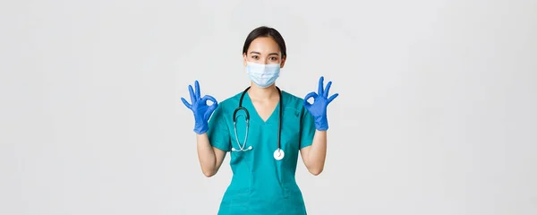 Covid-19, onemocnění koronavirem, koncept zdravotnických pracovníků. Usmívající se profesionální a sebevědomý asijský lékař, lékař v lékařské masce, rukavice a drhnutí ukazují v pořádku gesto, zaručit kvalitu služeb — Stock fotografie
