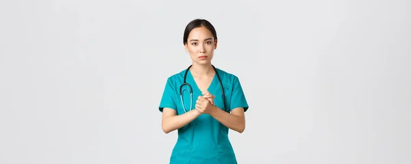 Covid-19, healthcare workers, pandemic concept. Hopeful serious-looking asian nurse, doctor asking something with concerned face, clench hands together in support during coronavirus, white background — Stock Photo, Image