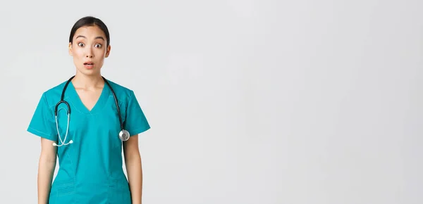 Covid-19, profissionais de saúde, conceito pandémico. Impressionado e surpreso asiático enfermeira em esfrega cair mandíbula e olhar para câmera sem palavras, olhando espantado sobre fundo branco — Fotografia de Stock