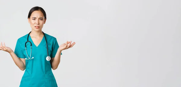 Covid-19, pracownicy służby zdrowia, koncepcja pandemii. zdezorientowana i rozczarowana azjatycka pielęgniarka, lekarka w fartuchu rozkłada ręce na boki i wzrusza ramionami zaniepokojona, nie może zrozumieć, pytając dlaczego — Zdjęcie stockowe