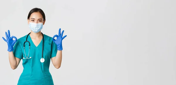 Covid-19, onemocnění koronavirem, koncept zdravotnických pracovníků. Usmívající se profesionální a sebevědomý asijský lékař, lékař v lékařské masce, rukavice a drhnutí ukazují v pořádku gesto, zaručit kvalitu služeb — Stock fotografie