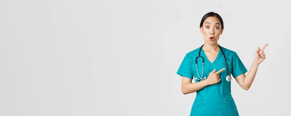 Covid-19, 의료 종사자, 전염병같은 개념. 충격을 받고 놀란 동양 여성 치료사, 손가락을 오른쪽 위로 향하는 수술복을 입은 의사, — 스톡 사진