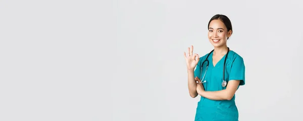 Covid-19, sjukvårdspersonal, pandemikoncept. Självsäker professionell asiatisk läkare, kvinnlig läkare i buskar, visar okej gest, garantera kvaliteten på tjänsterna på sjukhuset, godkänna och godkänna — Stockfoto
