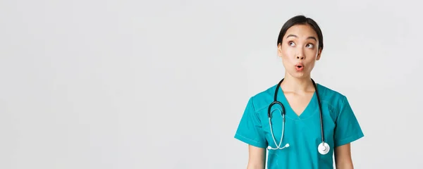Pracownicy służby zdrowia, zapobieganie wirusom, koncepcja kampanii kwarantanny. Imponujący i zdumiony azjatycki lekarz, pielęgniarka w medycznym fartuchu patrząc w lewym górnym rogu zadowolony, białe tło — Zdjęcie stockowe