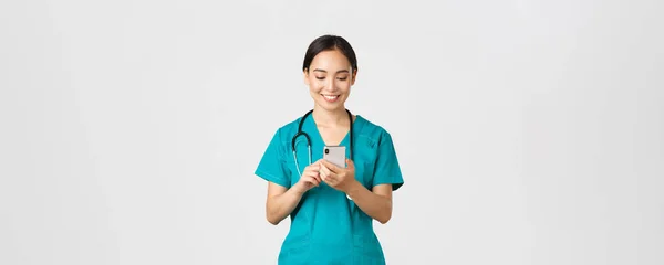 Covid-19 、医療従事者とウイルスの概念を防止します。笑顔の幸せな美しいアジアの女性のインターン,医師は電話をかけます,喜んで携帯電話の画面を見て,メッセージやアプリを使用して. — ストック写真