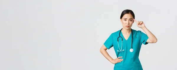 Covid-19, zdravotníci, pandemický koncept. Otravný skeptický asijské žena zdravotní sestra nebo lékař pokárat někoho hrát šílený nebo hloupý, roll prst přes spánek s odsuzující tvář — Stock fotografie