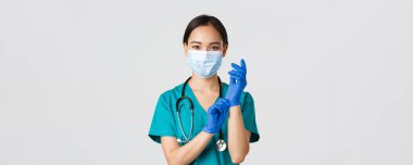 Covid-19, koronavirüs hastalığı, sağlık çalışanları konsepti. Profesyonel gülümseyen Asyalı kadın doktor, tıbbi maske ve önlüklü doktor, lastik eldiven giyin ro muayene, beyaz arka plan