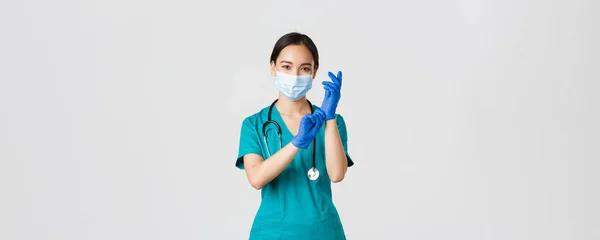 Covid-19, coronavirus ziekte, gezondheidswerkers concept. Professionele en zelfverzekerde glimlachende Aziatische arts, verpleegkundige dragen rubberen handschoenen en medisch masker voor patiëntenonderzoek, witte achtergrond — Stockfoto