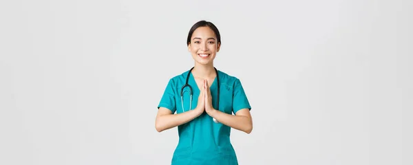 Covid-19, zdravotničtí pracovníci a prevence viru. Usmívající se krásná asijská sestřička, lékař v křoví s úsměvem, držet ruce u sebe přes hruď v namaste, pozdrav gesto — Stock fotografie