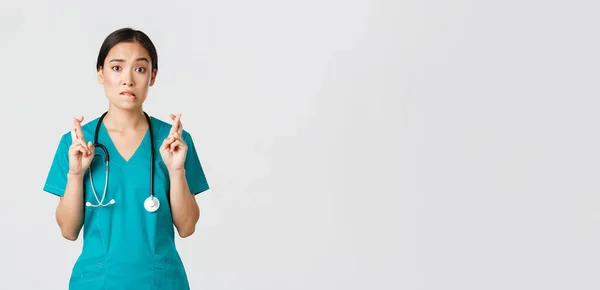 Covid-19, profissionais de saúde, conceito pandémico. esperançoso nervoso asiático feminino estagiário no scrubs espera para notícias, médico cruz dedos e mordendo lábio como olhando para câmera, orando — Fotografia de Stock
