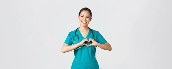 Covid-19, zdravotníci, pandemický koncept. Krásná péče asijský lékař, žena zdravotní sestra v drhnutí ukazuje srdeční gesto a usmívání, starat se o pacienty s láskou, bílé pozadí — Stock fotografie