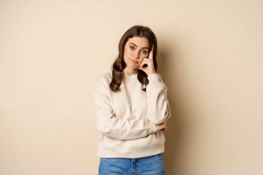 Annoyed woman, roll eyes and looking unamused, bothered and bored, standing over beige background
