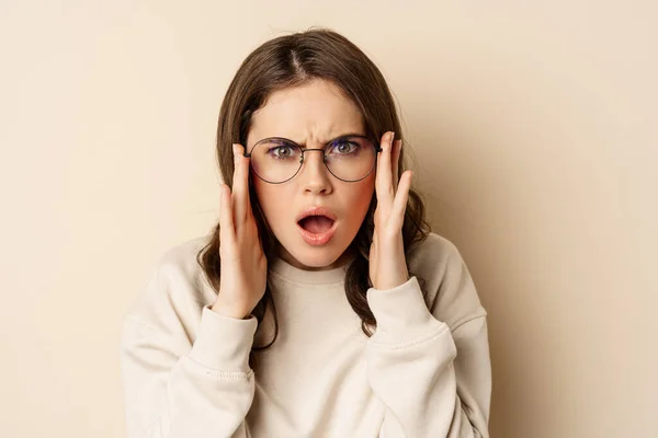 Close up portrait of woman in glasses looking confused and frustrated, cant understand smth strange, standing over beige background — Stock Photo, Image