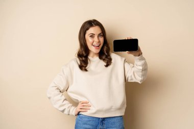 Gülümseyen güzel kadın model yatay akıllı telefon ekranı, mobil uygulama bej arka planda duruyor.