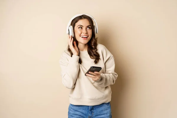 Happy kaukaska kobieta słuchanie muzyki w słuchawki na smartphone app, taniec i zabawy, stojąc nad beżowym tle — Zdjęcie stockowe